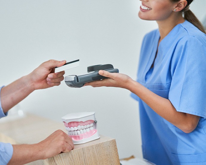 Woman in scrubs holding cardreader out for patient’s payment