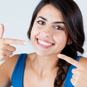 Woman with braided hair in blue shirt pointing to her smile with both hands